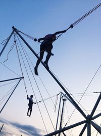 Low angle view of men hanging on rope against sky