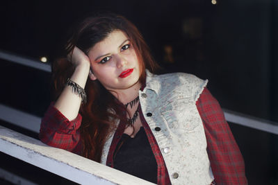 Portrait of beautiful woman with redhead leaning on railing at night