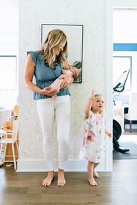 A mother holding a baby smiles at her toddler