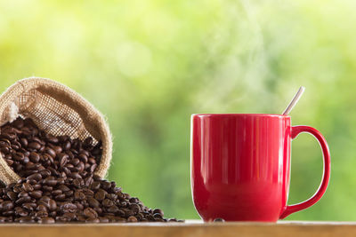 Coffee beans spilling from sack by red cup on table