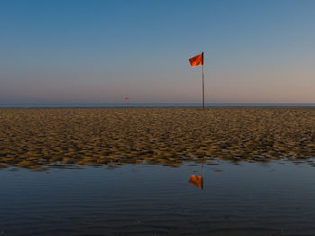 Red flag mirroring in water during morning hours at a beach in northern france