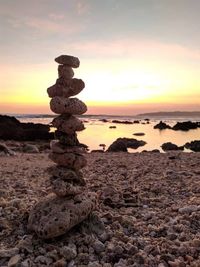 Stone stack on rocks at beach against sky during sunset