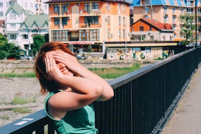 Happy woman covering face on road by railing in city