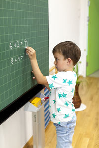 Cute boy writing on blackboard in classroom