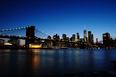 Illuminated bridge over river by buildings against clear sky at night