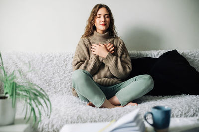 Beautiful young woman in lotus pose on bed practicing pranayama breathing techniques, finding inner