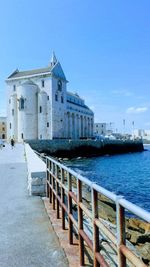 Buildings by sea against clear blue sky