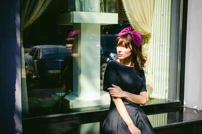 Beautiful young woman in black dress sitting on window