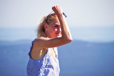 Young woman wearing sunglasses standing against sky