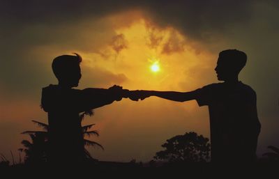 Silhouette people standing by tree against sky during sunset