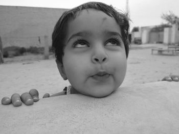 Close-up of cute baby girl making face looking up while standing by retaining wall