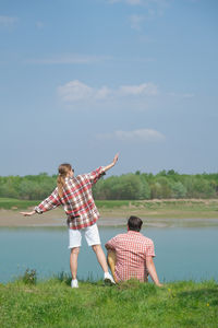Rear view of woman with arms outstretched standing by sea against sky