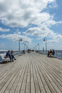 People sitting on pier by sea against sky