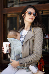 Woman wearing sunglasses carrying baby girl while sitting outdoors