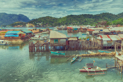 Boats moored in sea by houses against sky