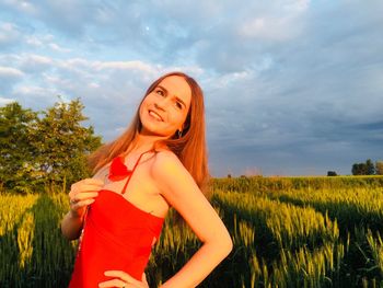 Smiling woman standing on field against cloudy sky