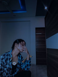 Portrait of young man sitting against wall at home