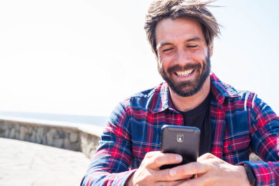 Portrait of smiling man using smart phone against sky
