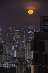 Illuminated buildings in city against sky at night full moon