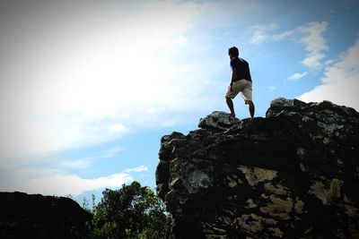 Low angle view of young man standing on rock formation against sky