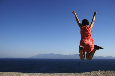 Woman jumping in front of sea against clear blue sky