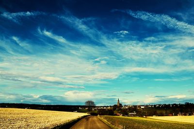 Road amidst field against sky