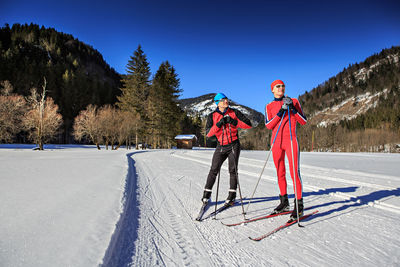 People skiing on snowy field against trees