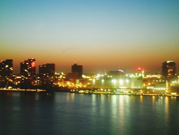 Illuminated city by river against sky at night