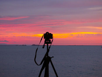 Silhouette of camera photographing sea against sky during sunrise 