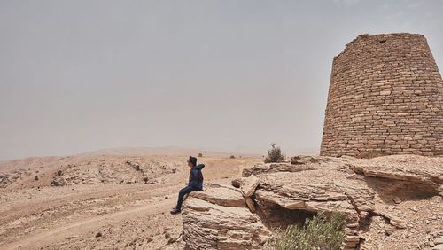 Man sitting on rock against clear sky