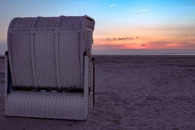 Hooded beach chair on shore against sky during sunset