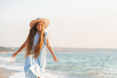 Smile blonde teenager girl 12-14 year old with long hair wear hat and elegant dress  over sea coast 
