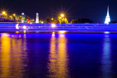 Illuminated light trails on river against sky at night