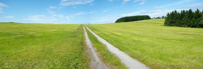 Road on grassy field against cloudy sky