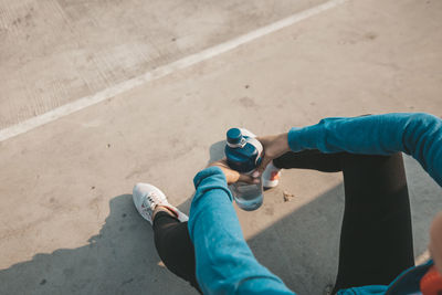 Low section of woman holding water bottle while sitting outdoors