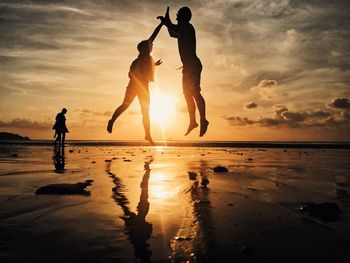 Silhouette friends jumping at beach against sky during sunset