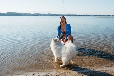 Cheerful woman playing with her snow-white dog breed japanese spitz on the city lake	
