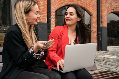 Smiling young woman using phone while sitting on laptop