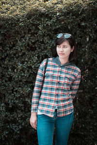 Thoughtful young woman looking away while standing against plants