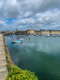 Boats moored at harbor by buildings against sky