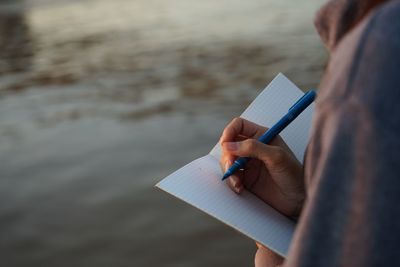 Midsection of man writing in book at sea