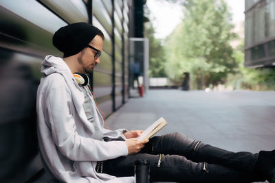 Side view of man reading a book while relaxing outdoors.