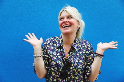 Cheerful young woman looking up against blue wall