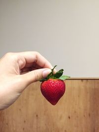 Cropped hand of woman holding strawberry against wall