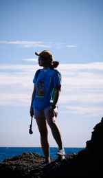 Young woman standing on rock by sea against sky