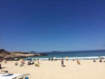 People on beach against clear blue sky