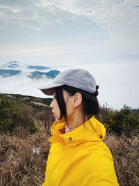 Side view of young woman standing against sky