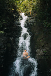 Man sitting on rock amidst waterfall