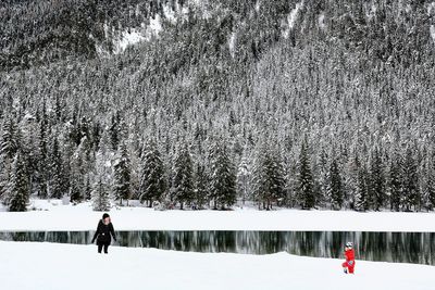 Woman standing on snow covered lake against trees