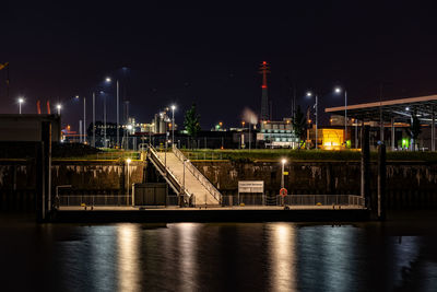 Illuminated building by river against sky at night